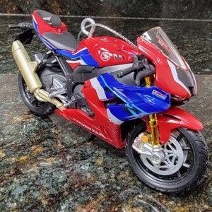 May include: A red, white, and blue Honda motorcycle model with gold accents. The motorcycle is a replica of a racing motorcycle.