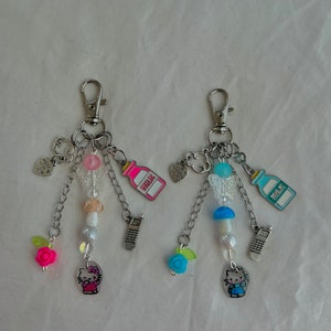 May include: Two silver charm keychains with Hello Kitty charms, pink and blue milk carton charms, and other charms. The charms are attached to silver chains with beads.