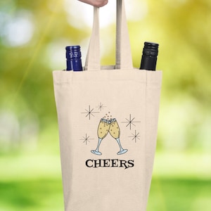 May include: A beige canvas wine tote bag with two bottle slots. The bag has a black design of two champagne glasses clinking with the word "CHEERS" below.
