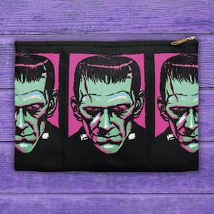 Könnte beinhalten: Schwarze Reißverschlusstasche mit einem sich wiederholenden Muster eines grünen und schwarzen Frankenstein-Monstergesichts auf rosa Hintergrund.