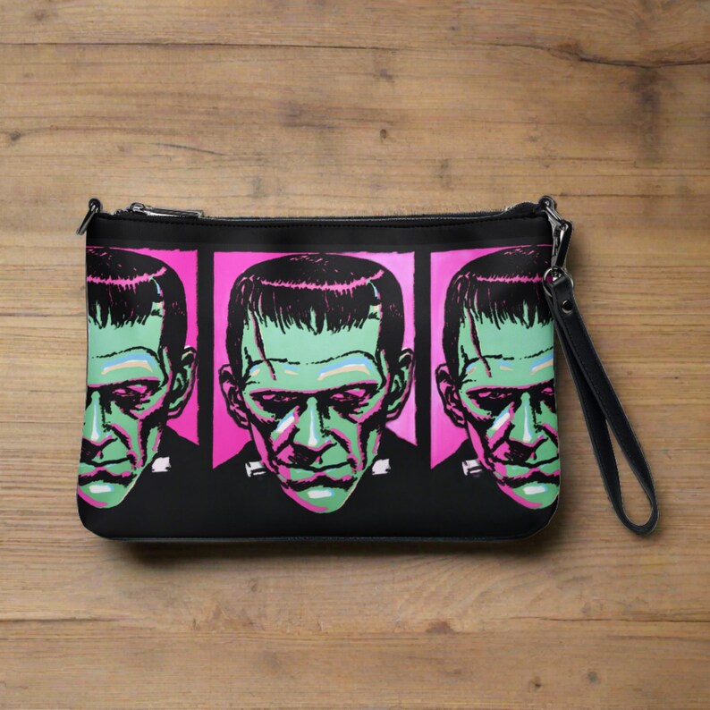 This black crossbody shoulder bag features a retro gothic print of Frankenstein's Monster with a green face and pink background. It's printed in a pattern on both sides.