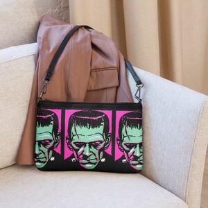 This black crossbody shoulder bag features a retro gothic print of Frankenstein's Monster with a green face and pink background. It's printed in a pattern on both sides.