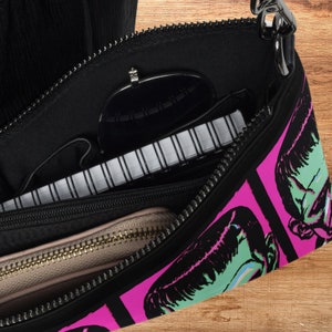 This shoulder crossbody purse converts to a large wristlet clutch. This purse features a retro Frankenstein Monster print of a green monster with a pink background.