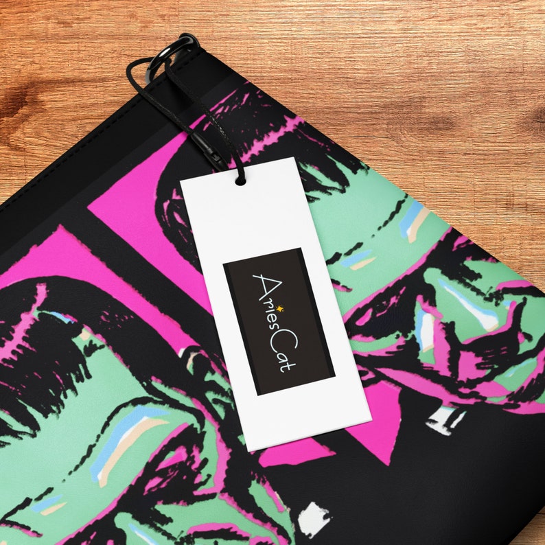 May include: Black and pink zippered pouch with a graphic print of two green and black Frankenstein-like faces. The pouch has a black tag attached with the text "AriesCat" in white.