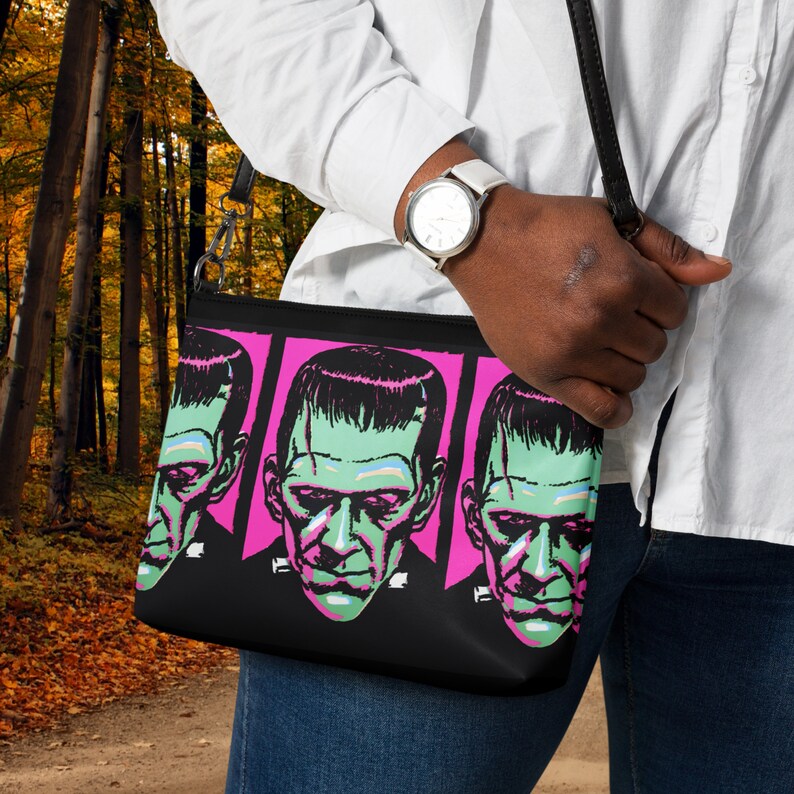 May include: A black crossbody bag with a pink and black design featuring three repeated images of a green-faced Frankenstein's monster.