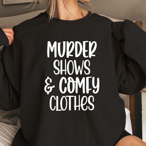 May include: Black sweatshirt with white text that reads 'Murder Shows & Comfy Clothes'