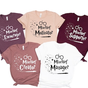 May include: Five t-shirts with different designs featuring a pair of glasses and a wand. The shirts are in various colors, including maroon, pink, white, and burgundy. The text on the shirts reads "Mischief Encourager", "Mischief Motivator", "Mischief Supporter", "Mischief Creator", and "Mischief Manager".