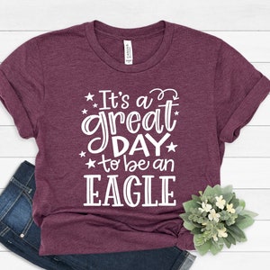 K&ouml;nnte beinhalten: Ein maroonfarbenes T-Shirt mit wei&szlig;em Text, der "It's a great day to be an EAGLE" lautet.