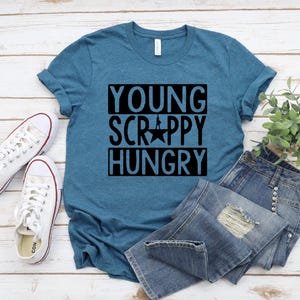 May include: A teal blue t-shirt with the text "Young, Scrappy, Hungry" in black lettering. The shirt has a star in the middle of the text.