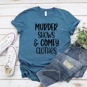 May include: A teal blue t-shirt with the text "Murder Shows & Comfy Clothes" printed in black.