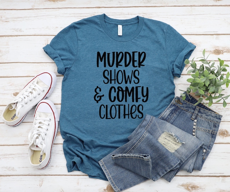 May include: A teal blue t-shirt with the text "Murder Shows & Comfy Clothes" printed in black.