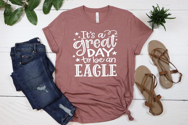 K&ouml;nnte beinhalten: Ein mauvefarbenes T-Shirt mit dem Text "It's a great day to be an EAGLE" in wei&szlig;en Buchstaben.
