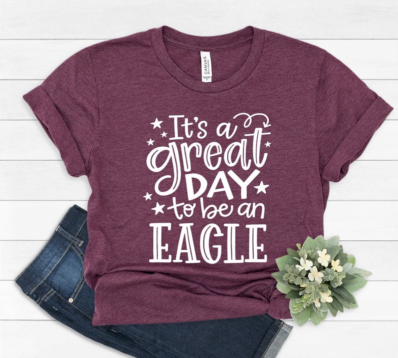 K&ouml;nnte beinhalten: Ein maroonfarbenes T-Shirt mit wei&szlig;em Text, der "It's a great day to be an EAGLE" lautet.