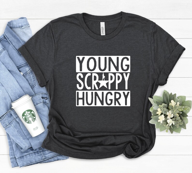 May include: Dark gray t-shirt with white text that reads "YOUNG SCRAPPY HUNGRY" with a white star and a silhouette of a person standing on the star.