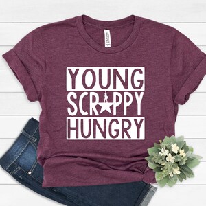 May include: A maroon t-shirt with the text "YOUNG SCRAPPY HUNGRY" in white letters. The text is in a bold, blocky font.