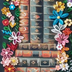 May include: A paper quilling artwork depicting a stack of old books in shades of brown and teal. The books are framed by a colourful floral border with yellow, pink, blue, and white flowers and green leaves.