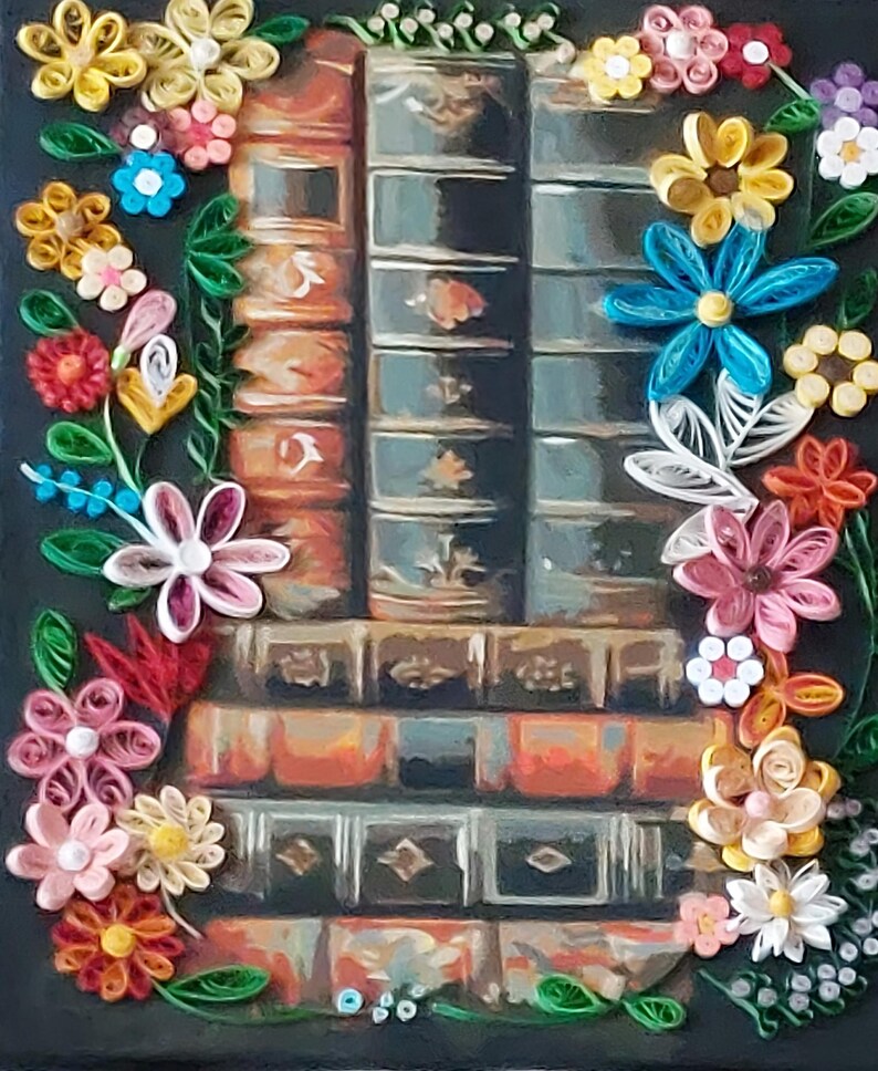 May include: A paper quilling artwork depicting a stack of old books in shades of brown and teal. The books are framed by a colourful floral border with yellow, pink, blue, and white flowers and green leaves.