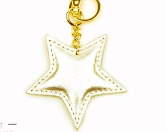 May include: Gold star-shaped leather keychain with a gold metal chain and clasp. The keychain is on a white background.