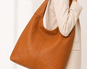 May include: A large, tan-colored hobo-style shoulder bag crafted from a textured material. The bag features a slouchy, unstructured silhouette with a single wide strap that integrates seamlessly into the body, providing a spacious interior.