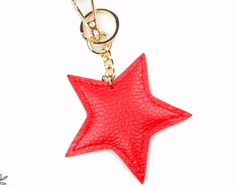 May include: A red leather star keychain with a gold chain and a gold clasp. The keychain is attached to a key ring.