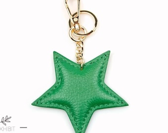 Puede incluir: Llavero de cuero verde en forma de estrella con un anillo y una cadena de metal dorado. El llavero tiene el texto "EXHIBIT LEATHER" y "Welcome To A New Look" en la parte inferior.
