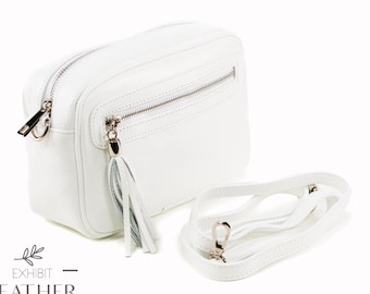 Puede incluir: Bolso bandolera de cuero blanco con cierre de cremallera y borla. El bolso tiene una correa larga ajustable.
