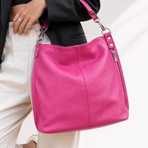 Peut inclure: Un sac hobo fuchsia vif à la surface texturée, doté d'une bandoulière unique fixée par des ferrures en métal argenté, d'une couture centrale verticale et d'une poche latérale zippée avec une tirette en métal argenté.
