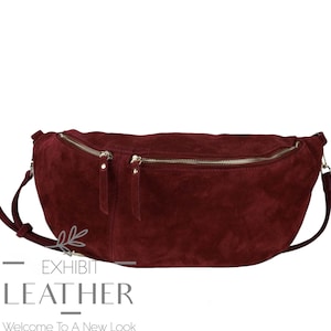 May include: A burgundy suede fanny pack with two zippered compartments and a silver-toned zipper. The bag has a long adjustable strap and the text "EXHIBIT LEATHER" and "Welcome To A New Look" in the bottom left corner.