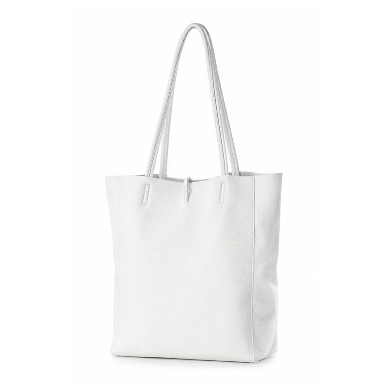 Pode incluir: Uma bolsa tote branca lisa com superf&iacute;cie texturizada e duas al&ccedil;as de ombro longas e finas. A bolsa apresenta um corpo retangular com base plana e detalhes de costura vertical onde as al&ccedil;as se prendem &agrave; borda superior do compartimento.
