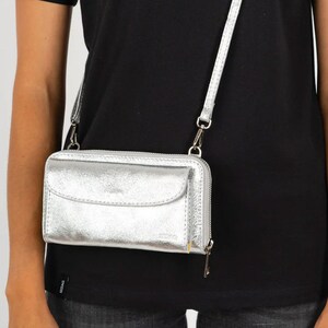 May include: A silver crossbody wallet with a zipper closure and a flap pocket. The wallet has a silver chain strap.