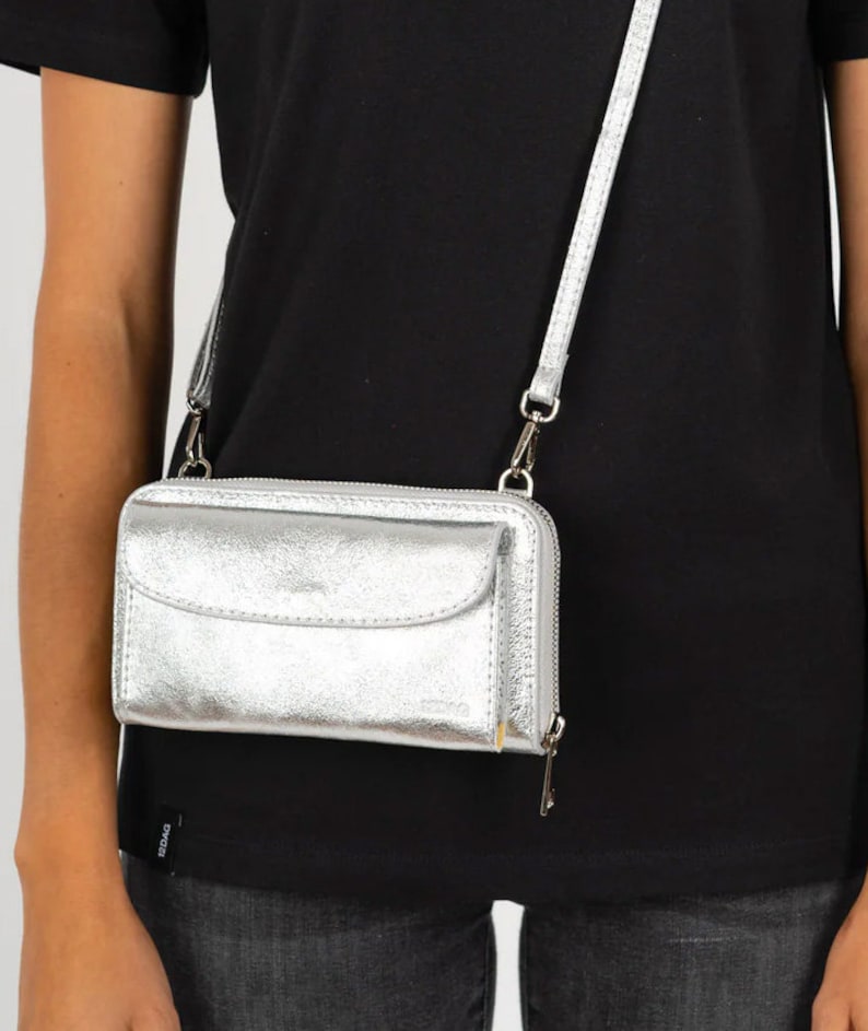 May include: A silver crossbody wallet with a zipper closure and a flap pocket. The wallet has a silver chain strap.