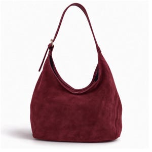 Op de afbeelding: Een diepbordeauxrode suède hobo-tas met een enkele schouderband en een verstelbare goudkleurige metalen gesp. De tas heeft een zacht, slungelig silhouet met een brede opening en een gladde, matte textuur over het gehele buitenoppervlak.