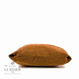 May include: A brown suede pillow with a soft, textured surface. The pillow is rectangular and has a slightly rounded edge.