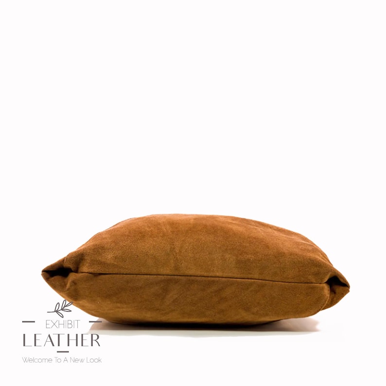 May include: A brown suede pillow with a soft, textured surface. The pillow is rectangular and has a slightly rounded edge.