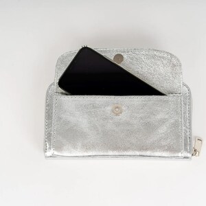 May include: A silver leather wallet with a zipper closure and a smartphone inside.