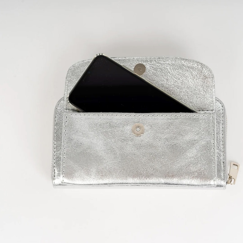 May include: A silver leather wallet with a zipper closure and a smartphone inside.