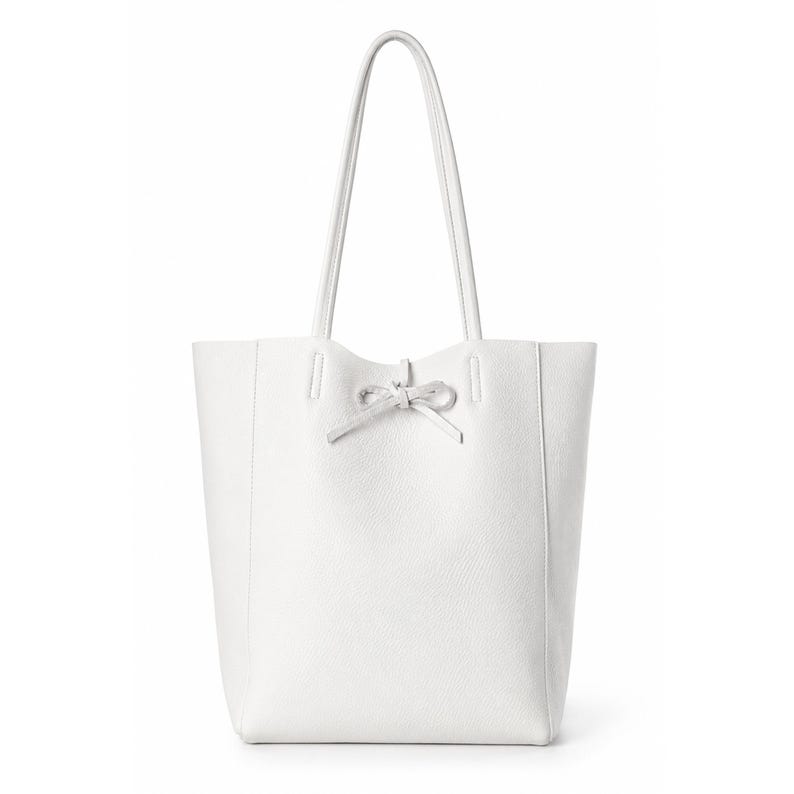 Pode incluir: Uma bolsa tote branca com superf&iacute;cie texturizada, apresentando duas al&ccedil;as longas de ombro e um detalhe de la&ccedil;o decorativo centralizado na abertura superior. A bolsa tem um formato retangular vertical estruturado com linhas limpas.