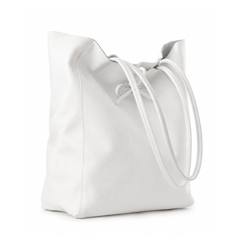 Pode incluir: Uma bolsa tote branca com superf&iacute;cie texturizada e silhueta macia e desestruturada. A bolsa possui duas al&ccedil;as de ombro longas e finas e um fecho de cord&atilde;o na parte superior central que se amarra em um pequeno la&ccedil;o, criando uma abertura.