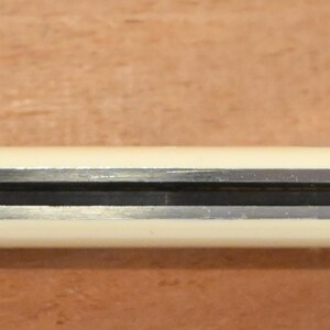 May include: A closed pocket knife with a cream-colored handle and a silver-colored blade. The knife is lying horizontally against a brown wooden surface. The blade is partially visible.