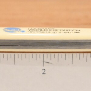 May include: A cream-colored pocket knife with a silver blade, measuring approximately 4 inches long. The knife has text that reads "Louisiana World Exposition New Orleans May 12-Nov 11 1984" and a blue logo.
