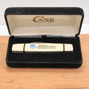 May include: A vintage Case XX pocket knife in a black velvet presentation box. The knife has a cream-colored handle with black accents and text that reads "Louisiana World Exposition New Orleans May 12-Nov 11 1984."