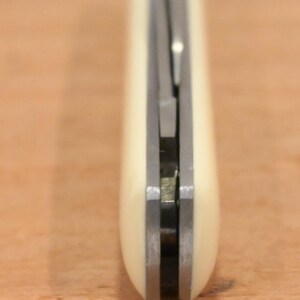 May include: Close-up of a pocket knife with a cream-colored handle and a silver blade. The knife is closed, showing the handle's smooth, rounded shape and the metal components. The blade is partially visible.