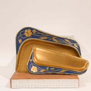 May include: Two nested metal trays with a gold interior and a deep blue border featuring gold floral patterns. The larger tray measures approximately 10 inches in width, while the smaller tray measures approximately 7 inches in width.
