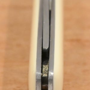 May include: Close-up of a knife with a cream-colored handle and a silver blade. The knife appears to be closed, with the blade tucked inside the handle. The handle has a rounded shape.