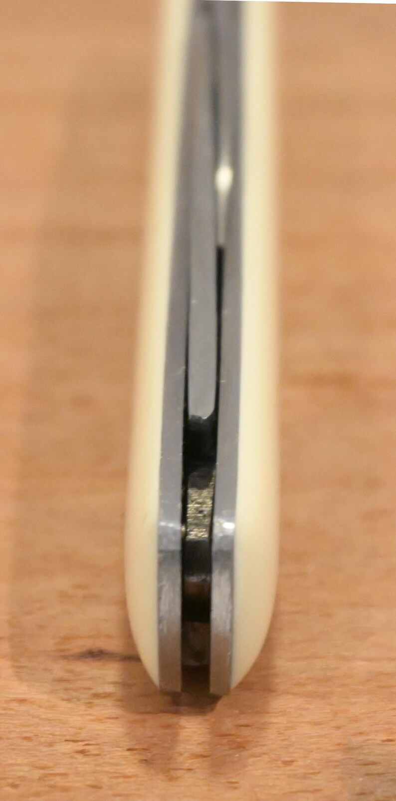 May include: Close-up of a knife with a cream-colored handle and a silver blade. The knife appears to be closed, with the blade tucked inside the handle. The handle has a rounded shape.