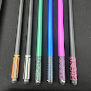 May include: Six pool cues with black shafts and various colored accents. The cues feature orange, silver, green, blue, pink, and black designs. Each cue has the word "Rage" printed on it, with the exception of one that has "2212".
