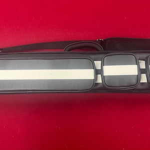 May include: A black and white pool cue case with a shoulder strap and handle. The case has a rectangular shape with white stripes and three pockets. The background is a solid red color.