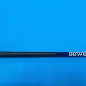 May include: A dark blue and black pen with the word "COWBOYS" in white lettering. The pen has a black grip and a white star logo. The pen is set against a bright blue background.