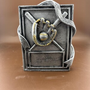 May include: Silver baseball trophy with a baseball glove, bat and ball design. The trophy has a blank space for engraving.