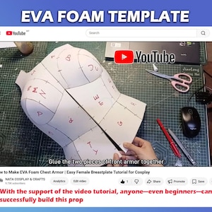 May include: A white EVA foam template for chest armor featuring red handwritten letters on each section. The template is displayed on a green cutting mat with scissors, a red pen, and a computer mouse visible in the background of the video frame.